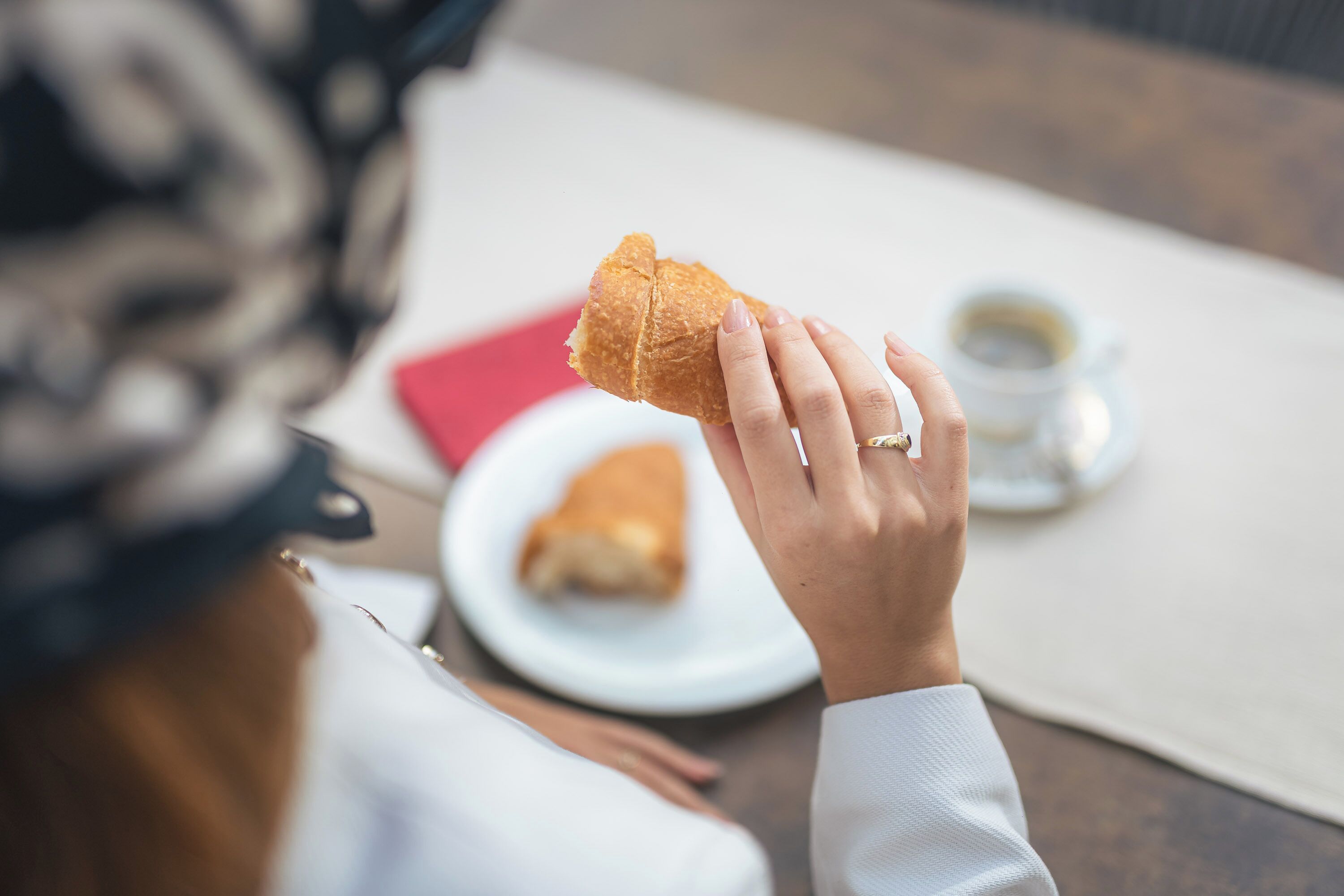 Una persona tiene in mano un pezzo di pane, su un tavolo con un piatto e una tazza di caffè.
