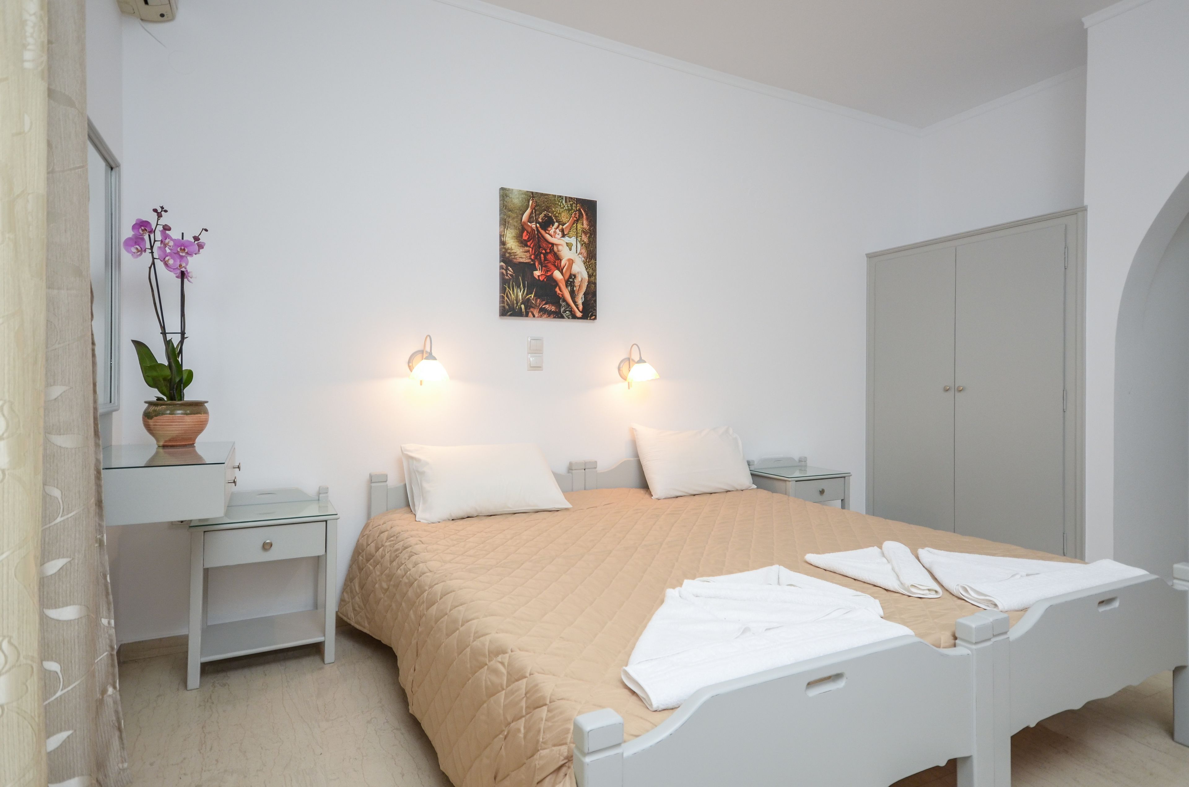 Un dormitorio con cama, mesitas de noche, cómoda y un cuadro en la pared, además de una orquídea en maceta.