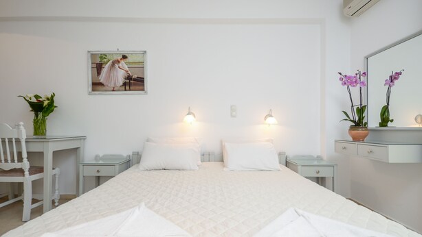 A hotel room with a large bed, two bedside tables, a desk, a chair, a potted plant, and a painting on the wall. - Golden Beach Studios (Naxos)