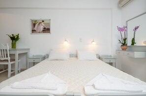 A hotel room with a large bed, two bedside tables, a desk, a chair, a potted plant, and a painting on the wall. - Golden Beach Studios (Naxos)