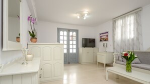 A spacious living room with a white sofa, a coffee table, a TV, and a door leading to another room. - Golden Beach Studios (Naxos)
