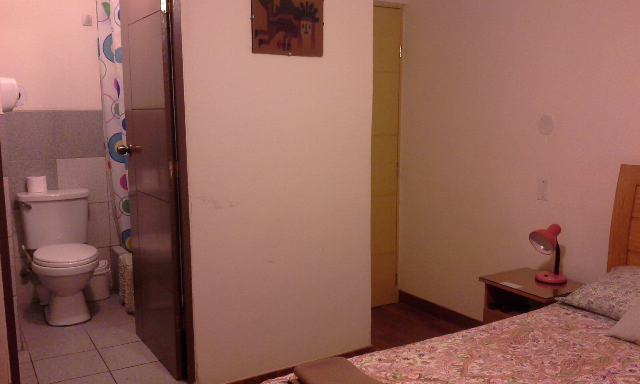 Una habitación pequeña y sencilla con inodoro, cama y mesita de noche.
