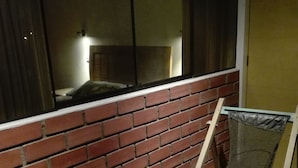 A balcony with a red brick wall, a metal chair, and a mesh screen. - Posada Peregrinus (Lima)