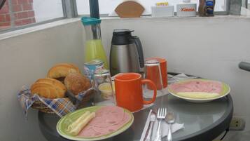 A breakfast table with croissants, ham, and eggs, along with orange mugs and silverware.