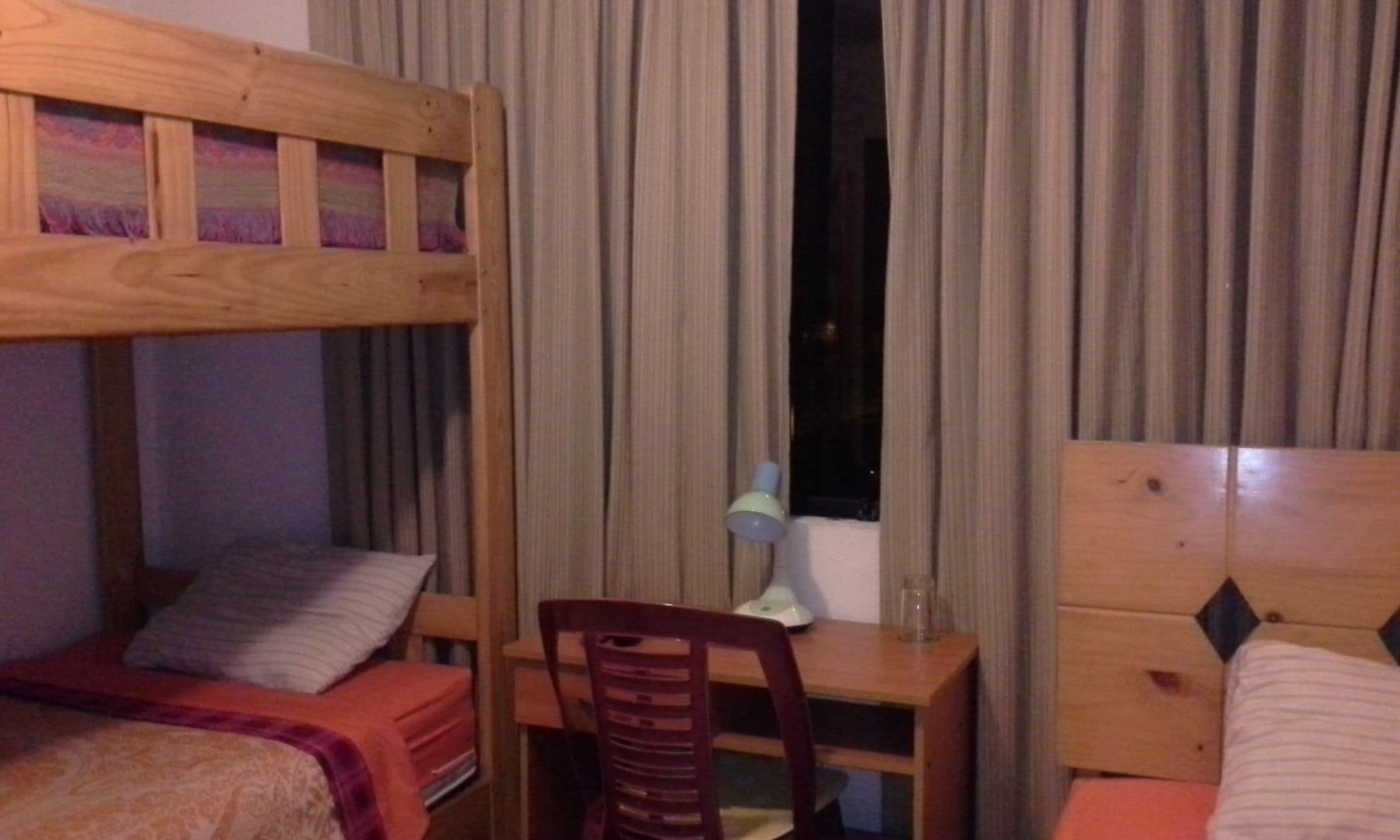 A room with a bunk bed, a desk with a chair, and a window with curtains.