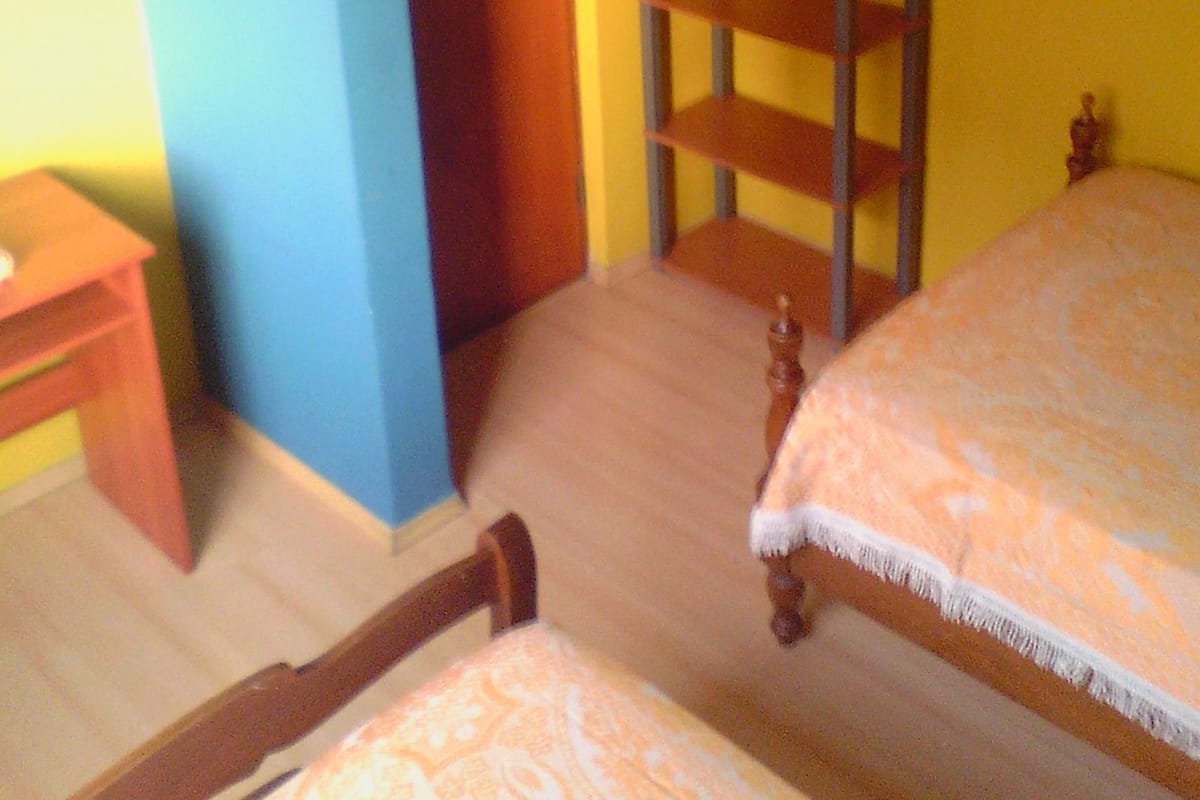 A room with two beds, a wooden shelf unit, a small table, and a door.