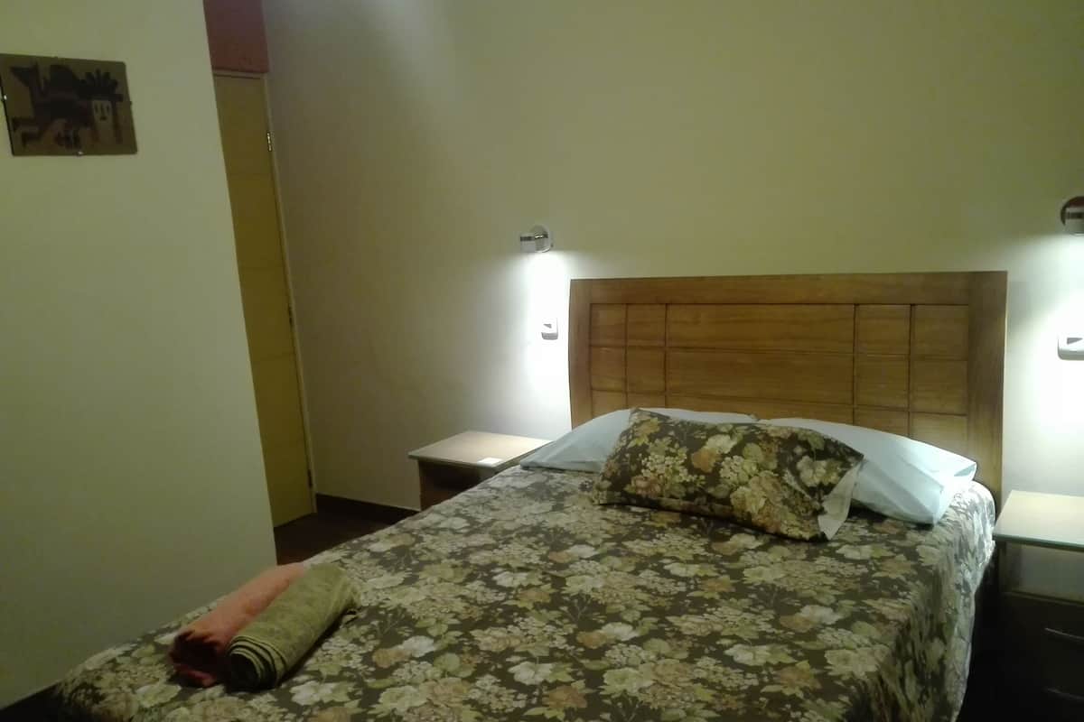 A neatly made bed with floral bedding, a wooden headboard, and a bedside table with a lamp.