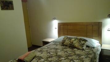 Una cama bien hecha con ropa de cama floral, cabecera de madera y mesita de noche con lámpara.