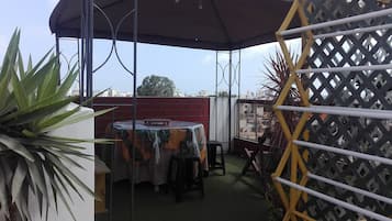 Een overdekt terras met een tafel en stoelen, omgeven door planten en een lattenhek.