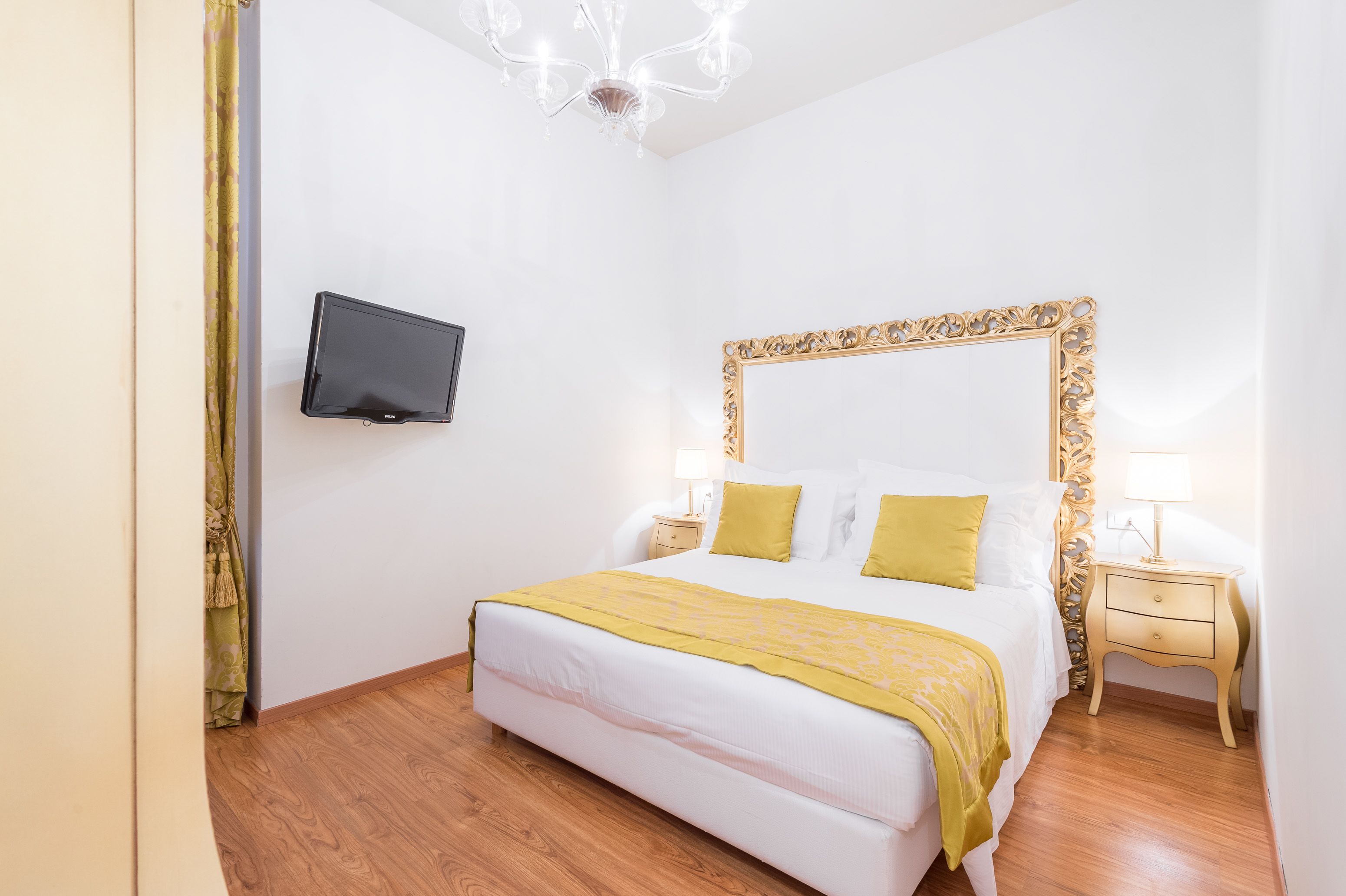Quarto de hotel bem arrumado, com uma cama grande, televisão na parede e um candelabro.