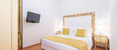 Quarto de hotel bem arrumado, com uma cama grande, televisão na parede e um candelabro.