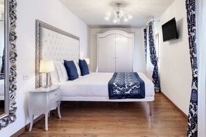 A hotel room with a large bed, a nightstand, a mirror, a television, and a chandelier. - Al Bailo di Venezia Apartments (Venice)