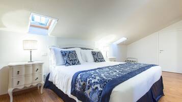A bedroom with a skylight, a bed with a blue and white bedspread, two bedside tables with lamps, and a wooden floor.