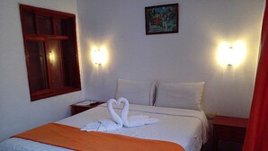 Una habitación de hotel con cama, dos lámparas fijadas a la pared, un cuadro y una ventana con marco de madera.