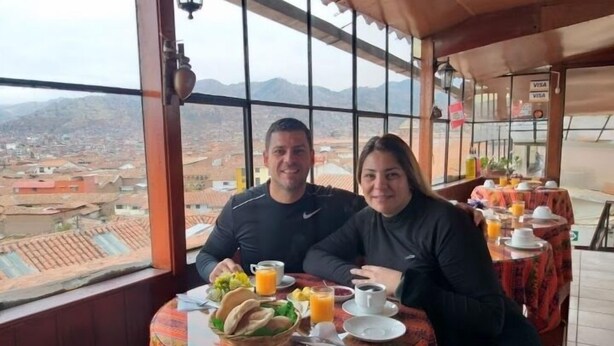 Una pareja cenando en una mesa con vistas a un paisaje urbano y montañas.