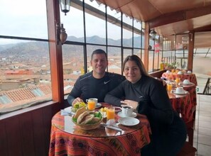 A couple dining at a table with a view of a cityscape and mountains. - Hostal Tu Hogar (Cusco)