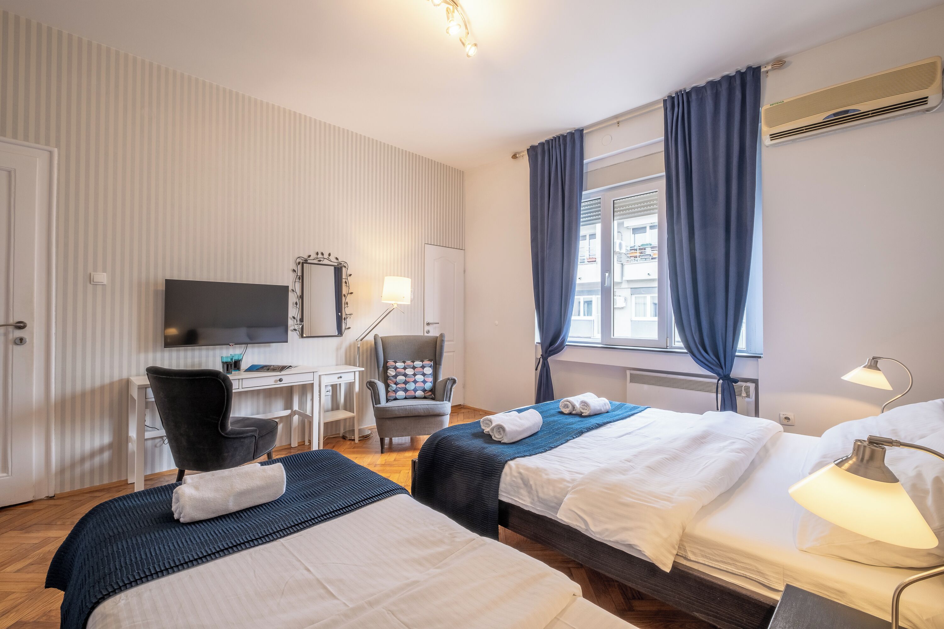 Una habitación de hotel con dos camas, un escritorio, una silla, un televisor y una ventana con cortinas.