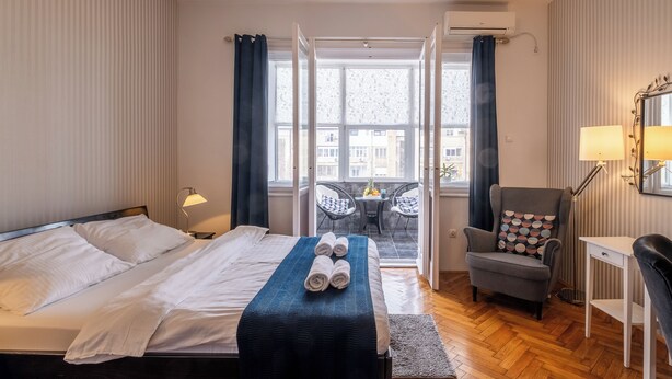 Ein Hotelzimmer mit Bett, Schreibtisch, Stuhl, einem Balkon mit Tisch und Stühlen sowie einer Klimaanlage.