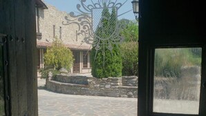 Una puerta abierta que da a un patio con suelo de piedra, una reja metálica decorativa y un edificio con fachada de piedra al fondo.