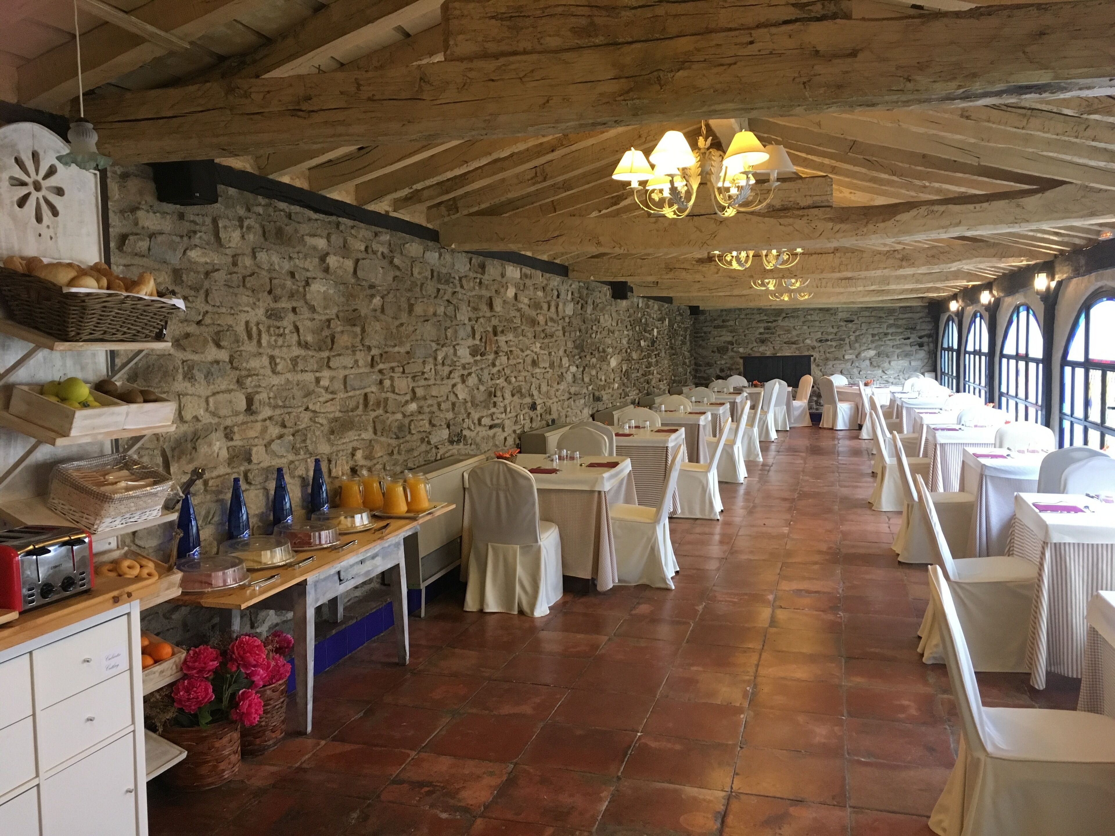 A spacious dining hall with stone walls, white tables, and chairs.