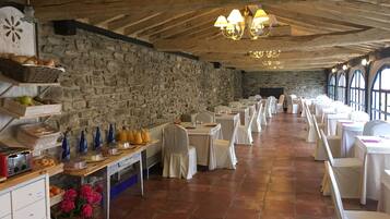 A spacious dining hall with stone walls, white tables, and chairs.