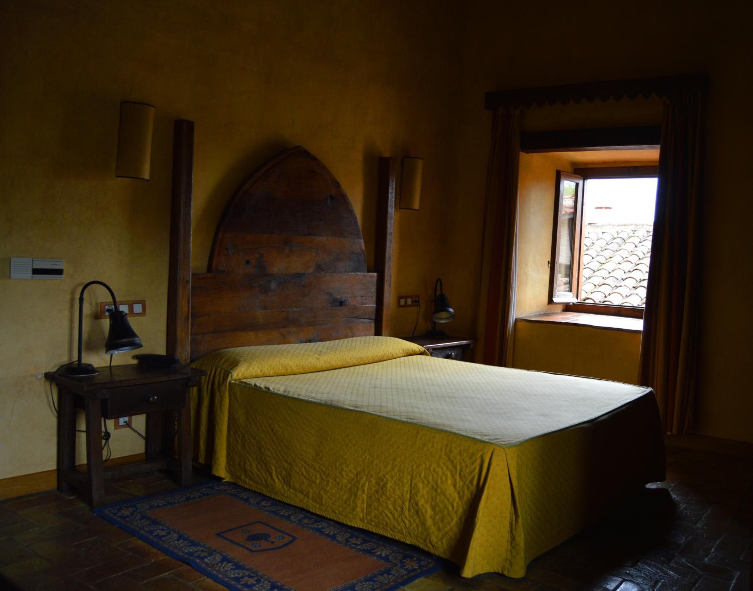 A bedroom with a bed, a desk, a lamp, and a window with curtains.