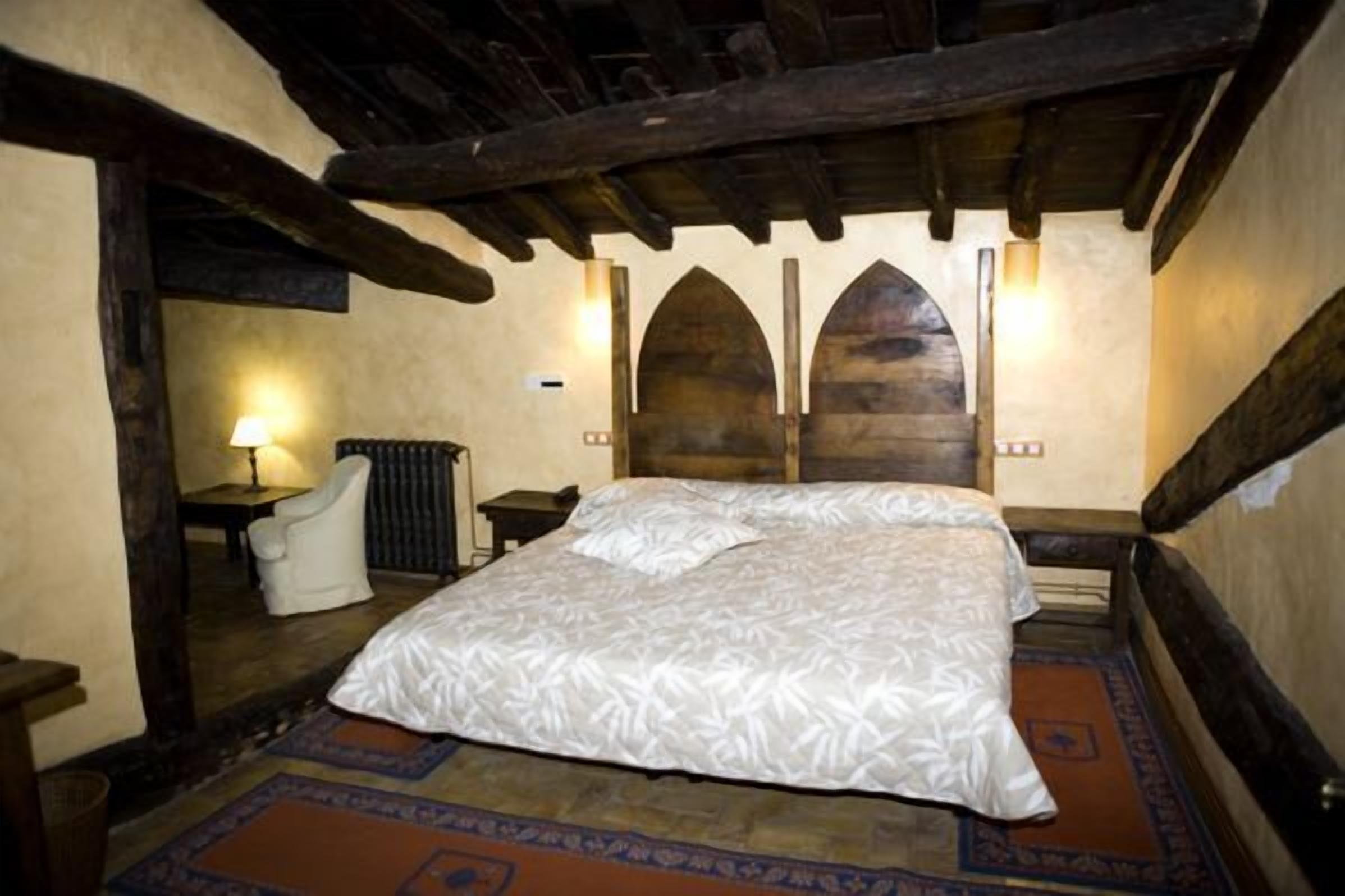 Una habitación con una cama grande, una silla, una lámpara y techo de madera.