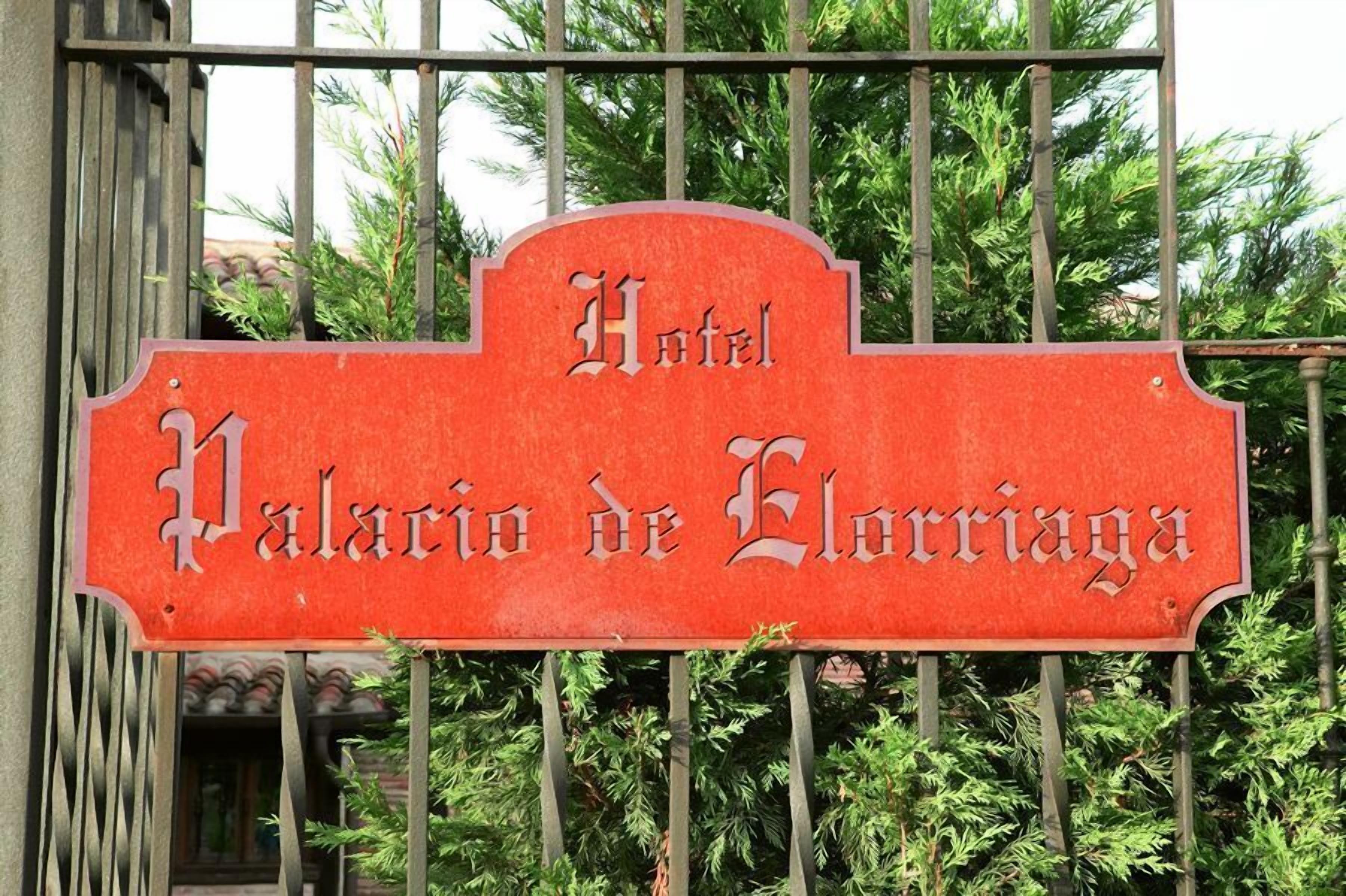 A red sign with the text "Hotel Palacio de Elorriaga" on a metal gate.
