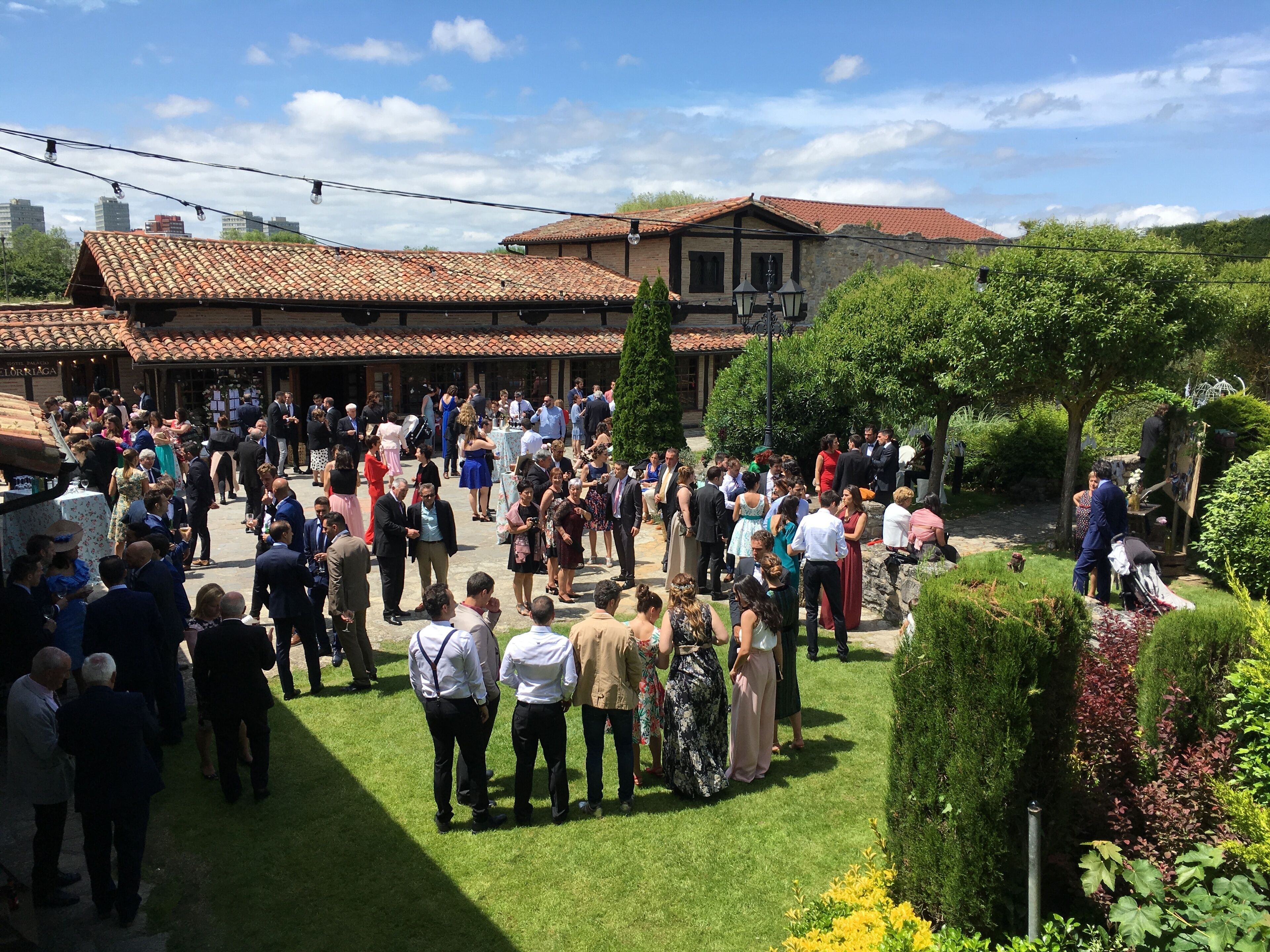 A courtyard with a crowd of people, surrounded by buildings with red-tiled roofs and a well-maintained lawn.