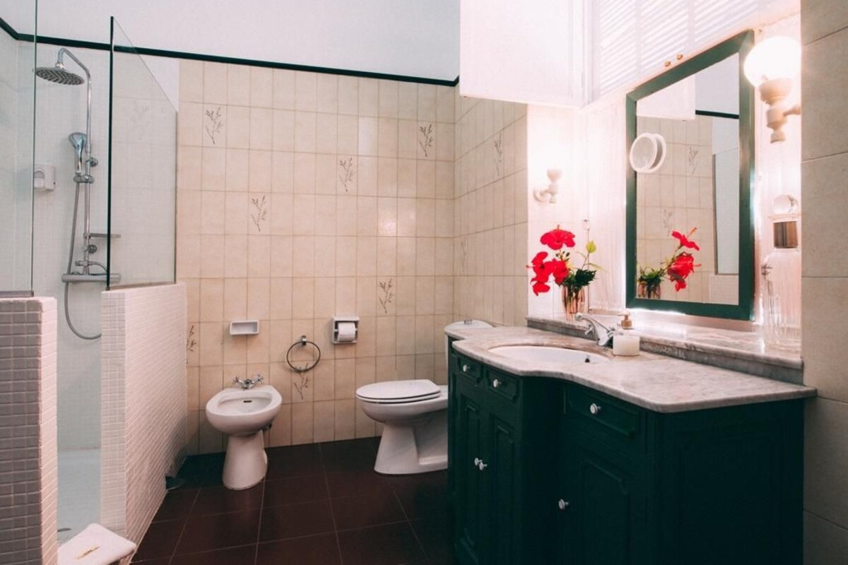 A bathroom with a shower, two toilets, a bidet, and a vanity with a mirror.