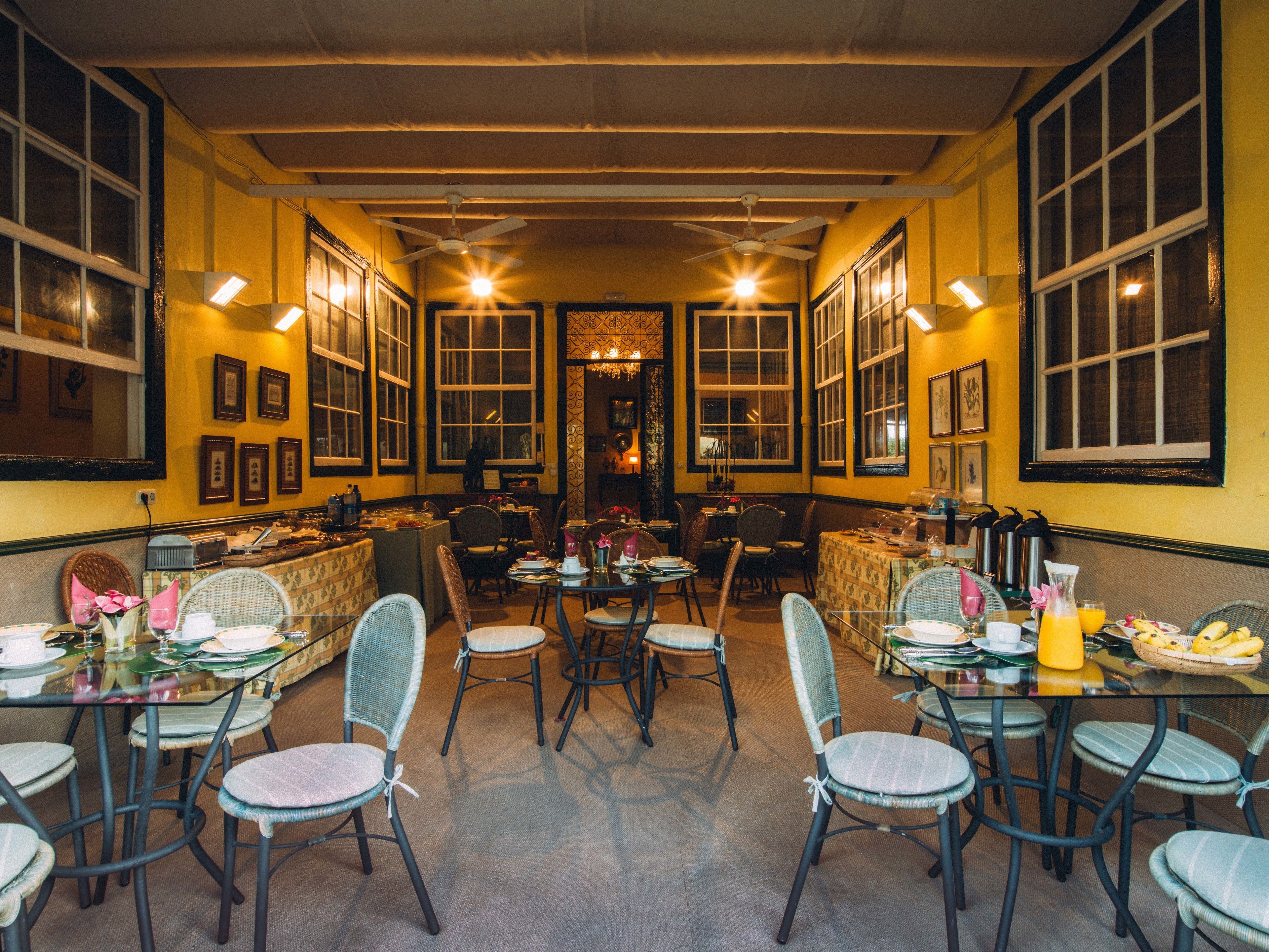 Een restaurant met meerdere tafels en stoelen, grote ramen en plafondventilatoren.
