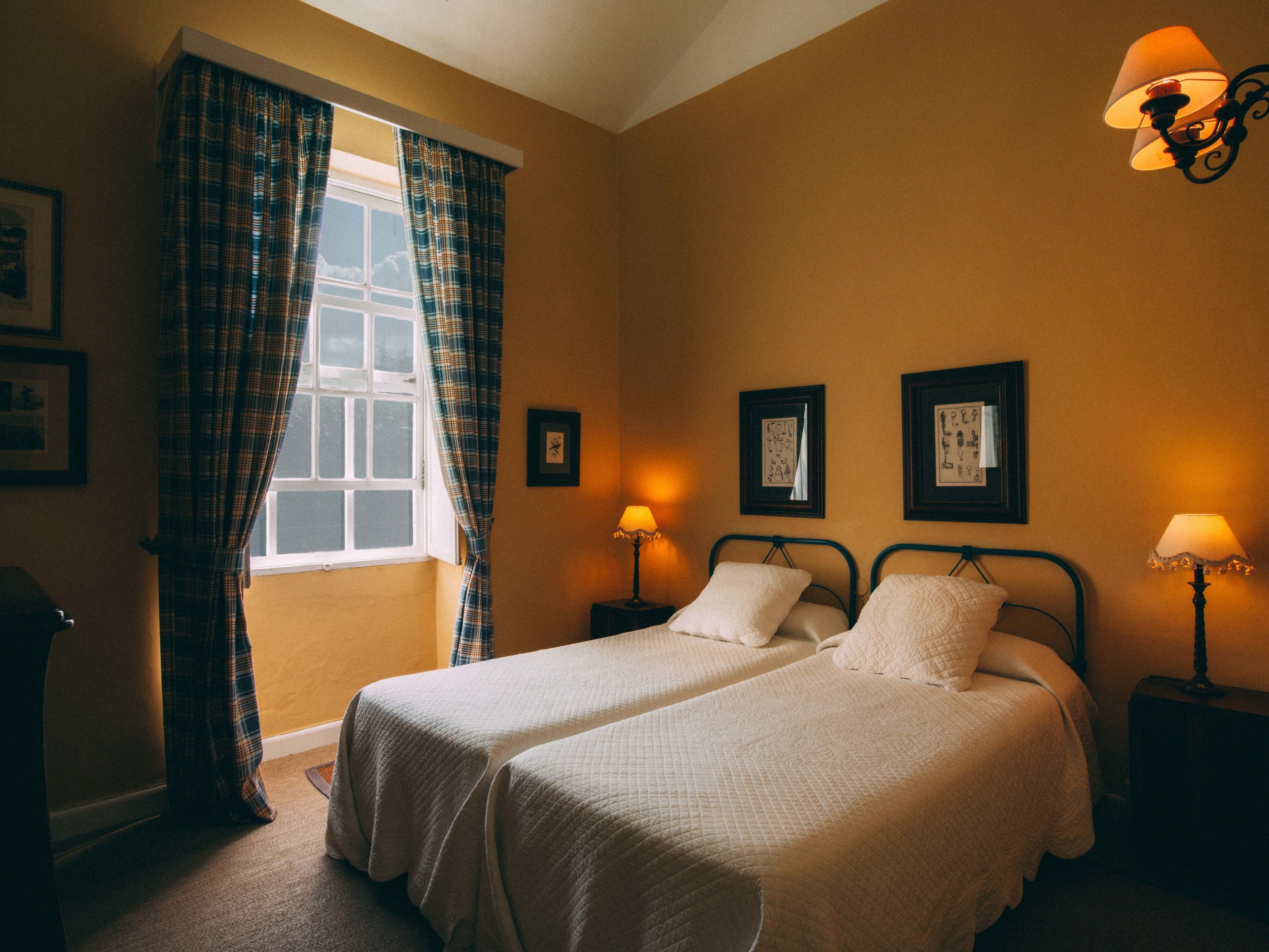A room with two beds, a window with plaid curtains, and wall-mounted lamps.