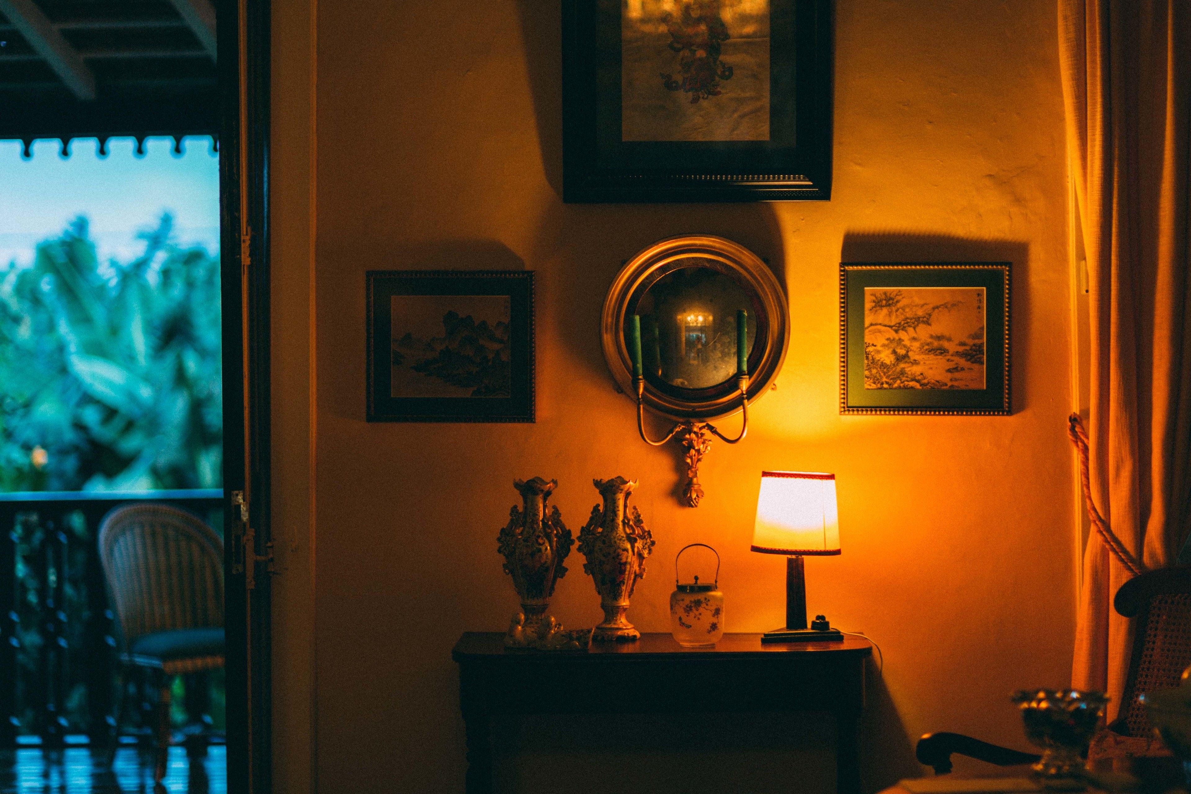Une pièce avec une petite table, une lampe, deux vases et des tableaux encadrés accrochés au mur.