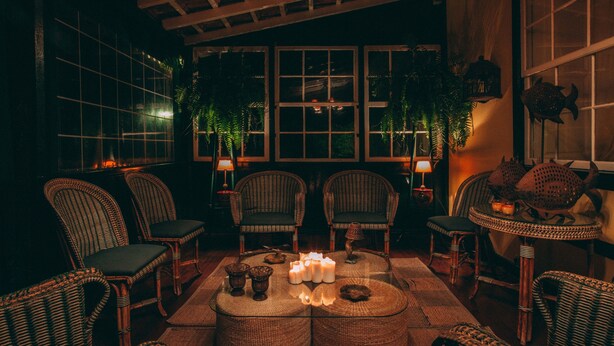 A cozy room with wicker furniture, a central round table with candles, and large windows with plants. - Hotel Rural Casamarilla (Garachico)