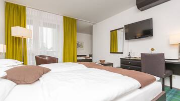 Habitación de hotel con cama, escritorio, silla, televisor y ventana con cortinas.