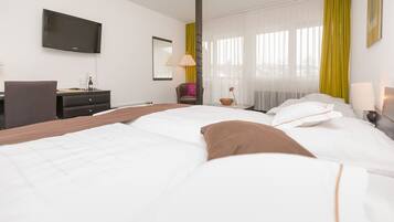 Habitación de hotel con cama, escritorio, silla, televisor y ventana con cortinas.