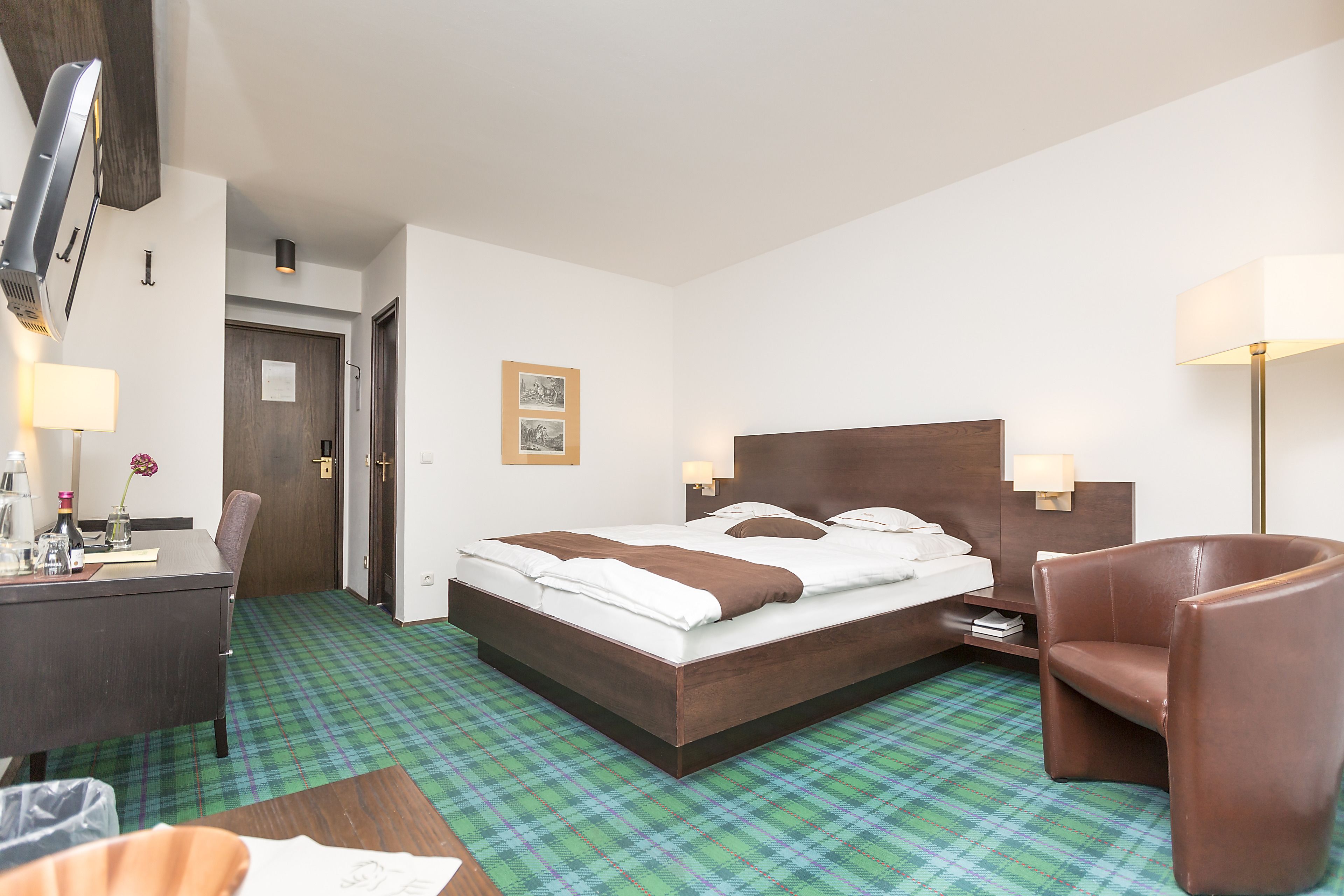 Una habitación de hotel con cama, escritorio, silla, mesita de noche y lámpara.