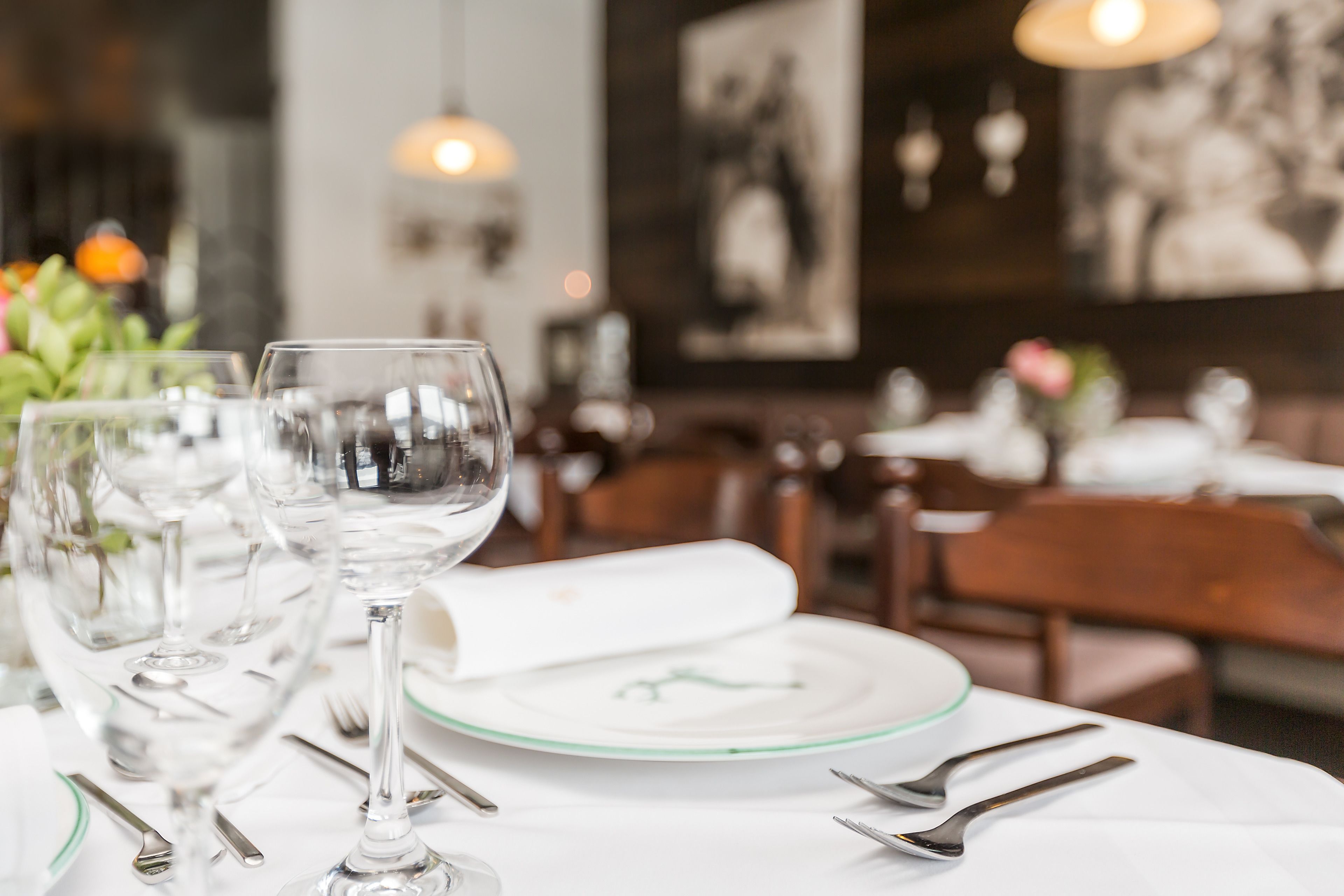 A dining table set with wine glasses, plates, and cutlery, with a blurred background of a restaurant interior.