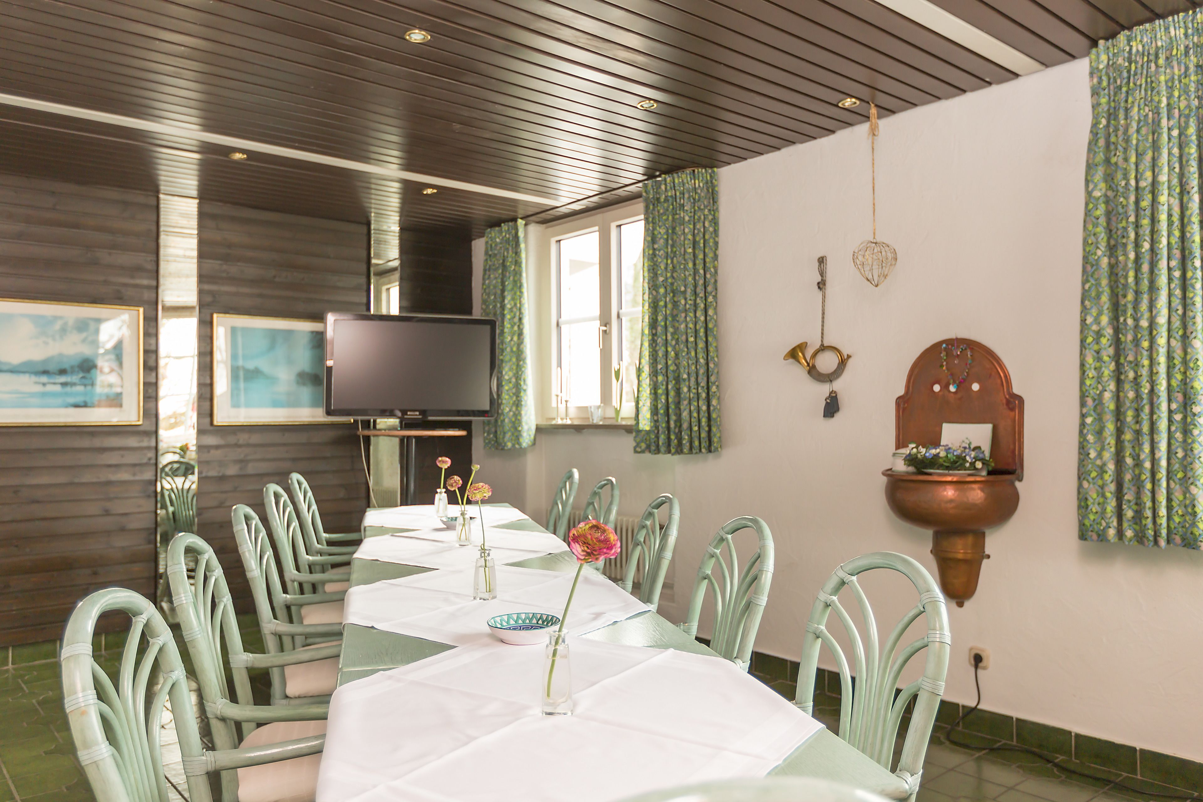 Un comedor con una mesa larga, sillas, un televisor y un lavamanos instalado en la pared.