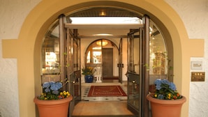 L’entrée d’un hôtel, avec une porte en verre, un tapis rouge et deux grands pots de fleurs.