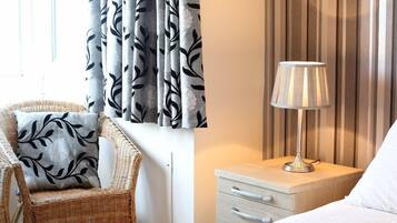 Een hotelkamer met een rieten stoel, een nachtkastje met een lamp, en een bed met wit beddengoed.