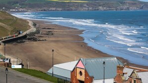 A coastal view with a sandy beach, a sea wall, and buildings with distinct architecture. - The Riviera Guest House (Whitby)