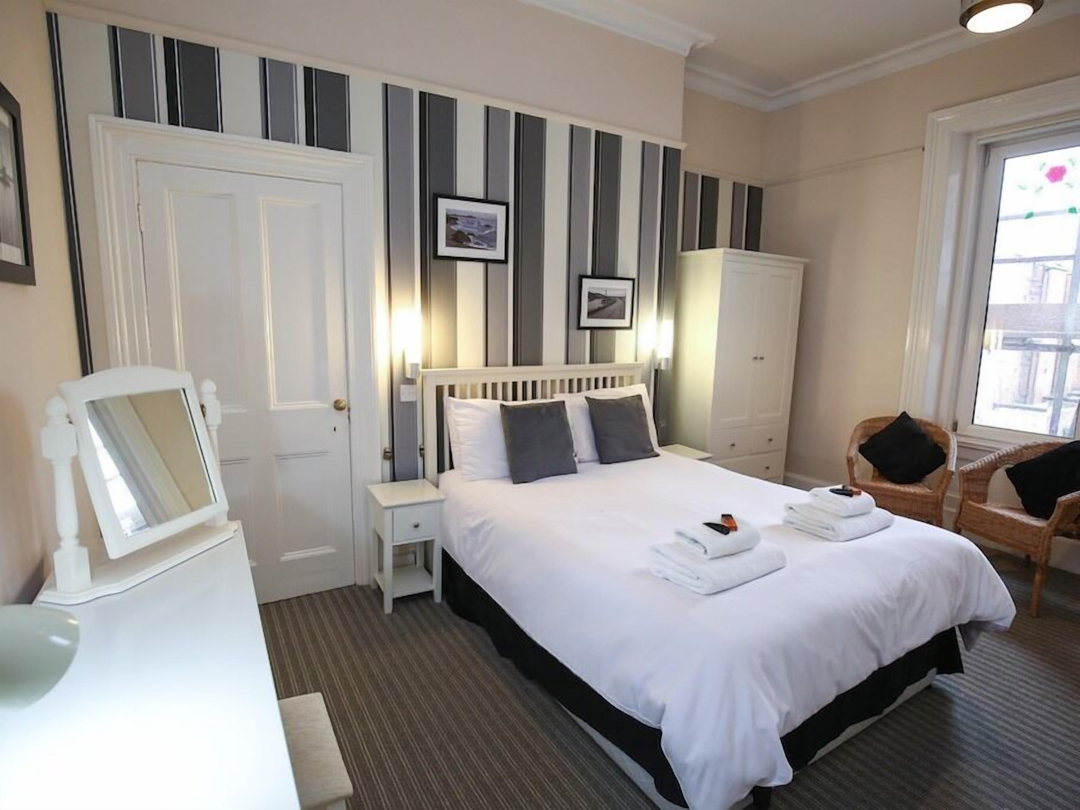 Ein Hotelzimmer mit einem großen Bett, einem Nachttisch, einem Kleiderschrank, einem Sessel und einem Fenster.