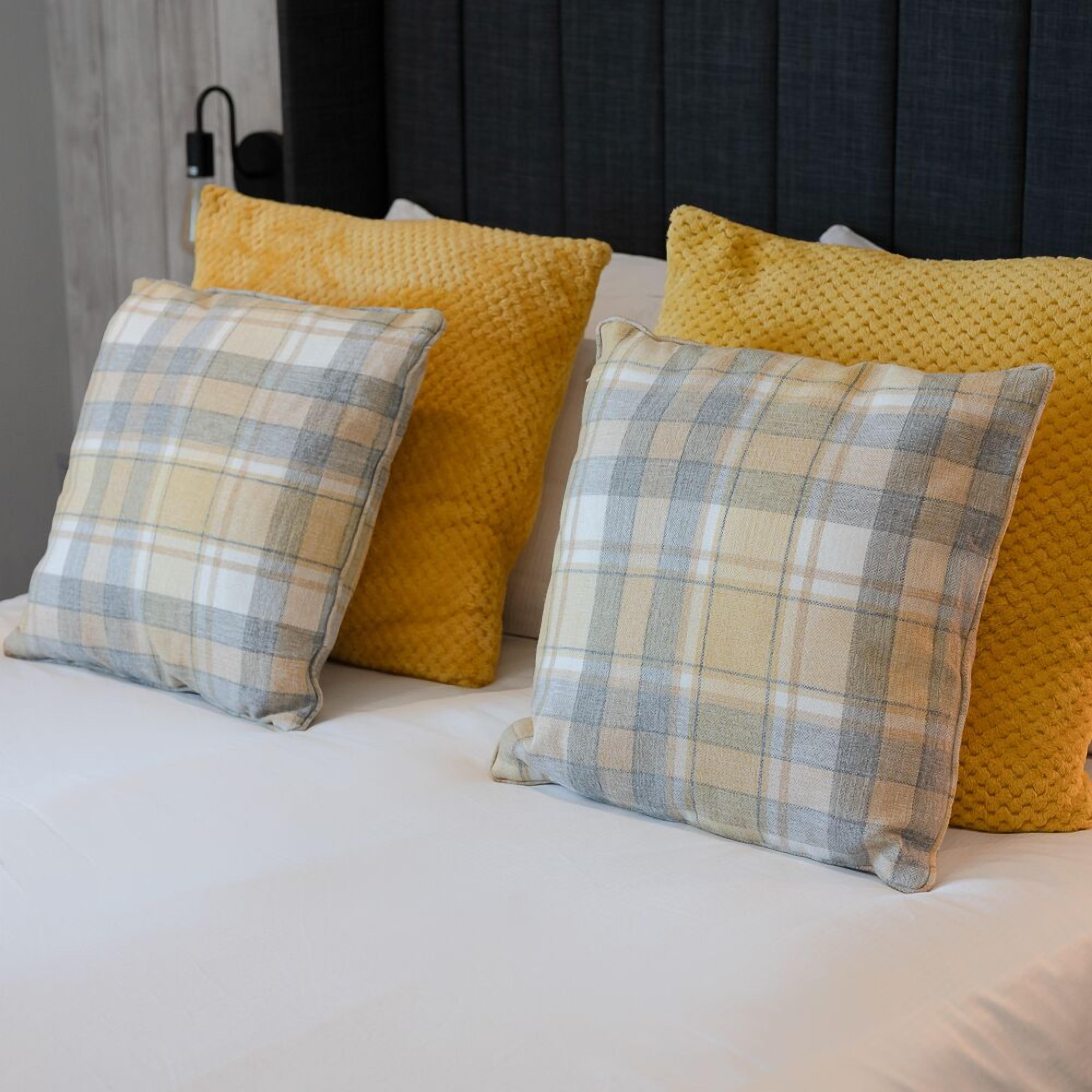 A bed with two pillows, one yellow and one plaid.