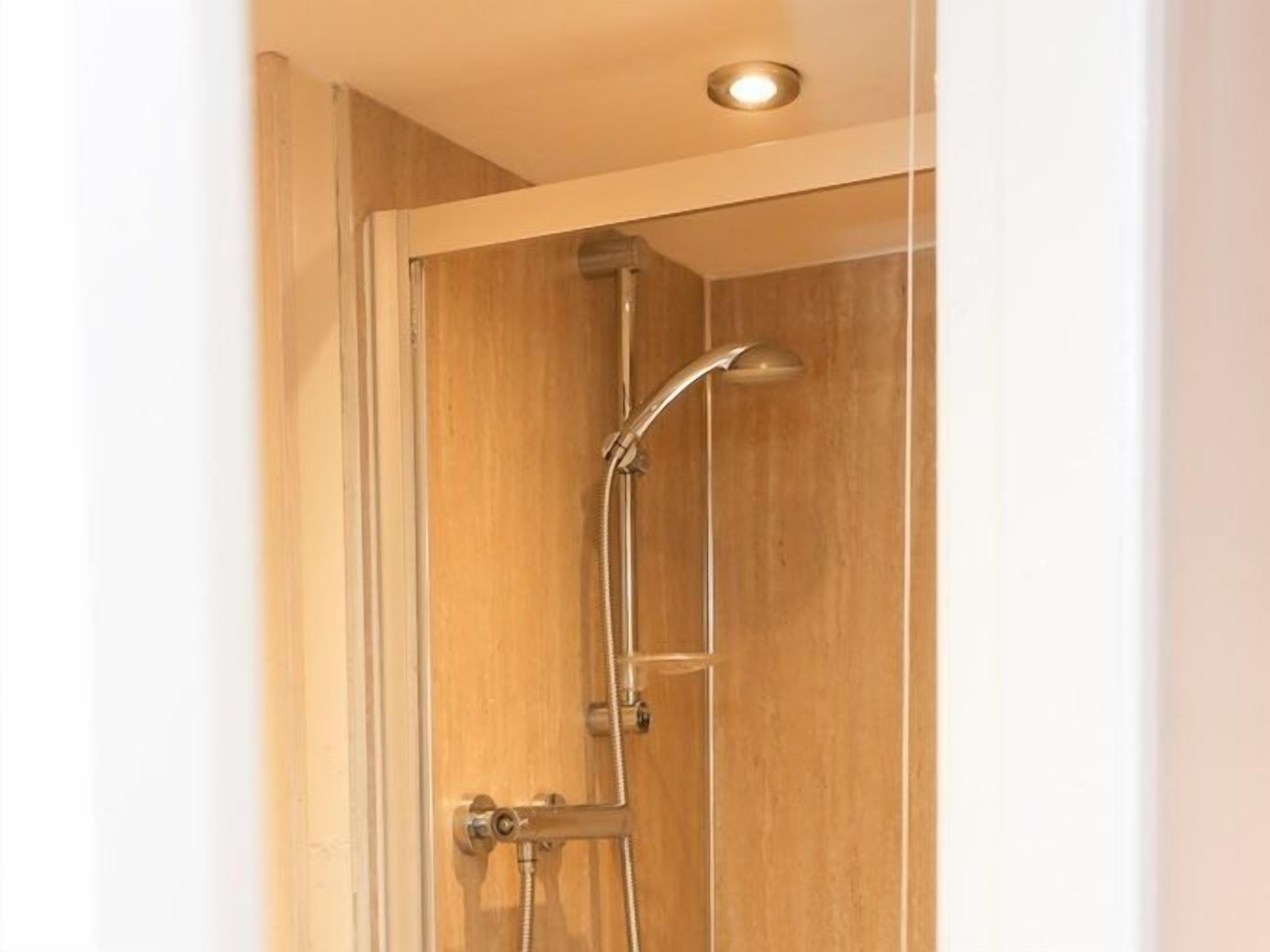 A shower with a glass door, a handheld showerhead, and a wall-mounted faucet.