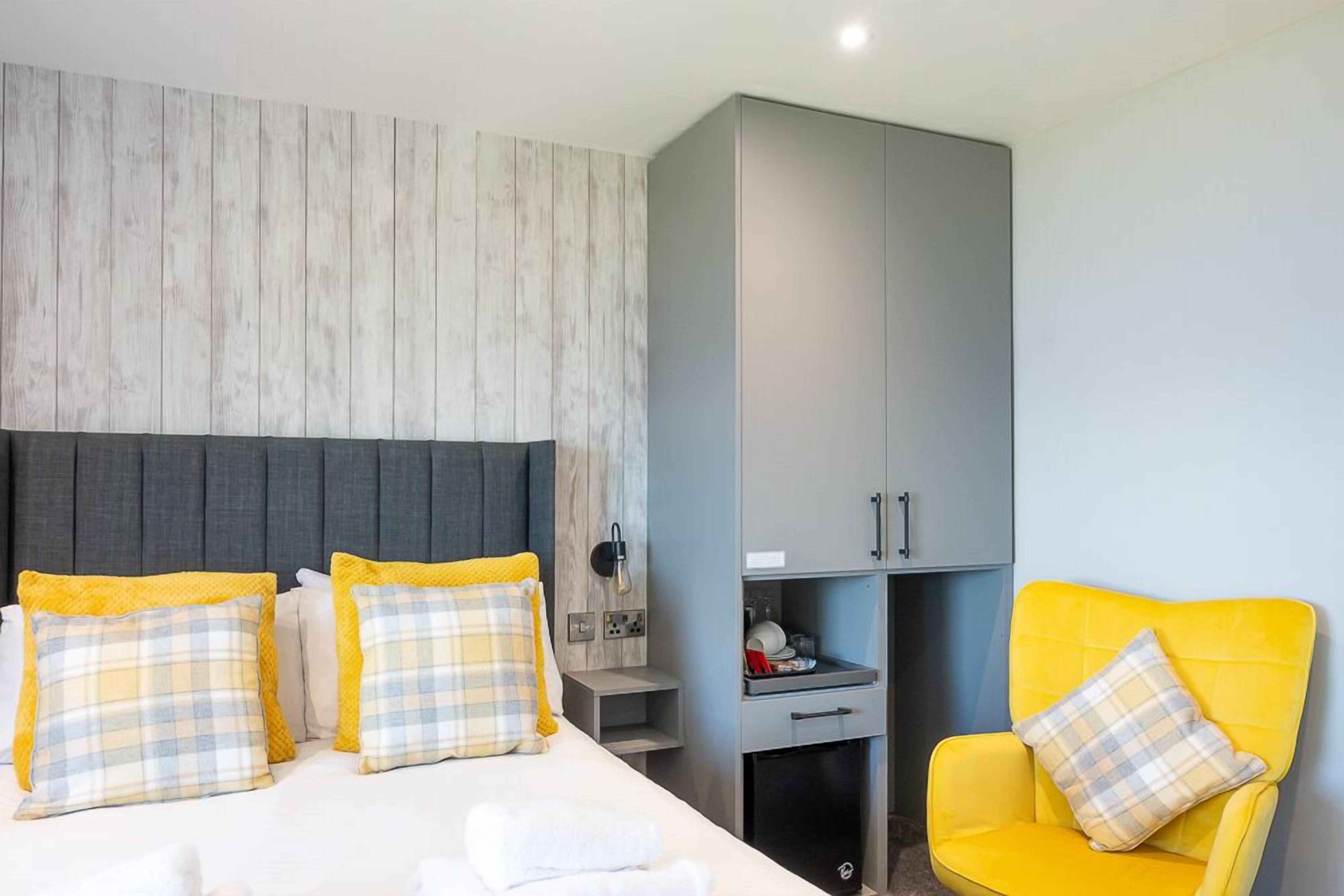 A hotel room with a bed, a chair, a wardrobe, and a small table.