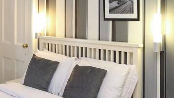Una cama con ropa blanca y dos almohadas, cabecera blanca y dos cuadros en la pared.