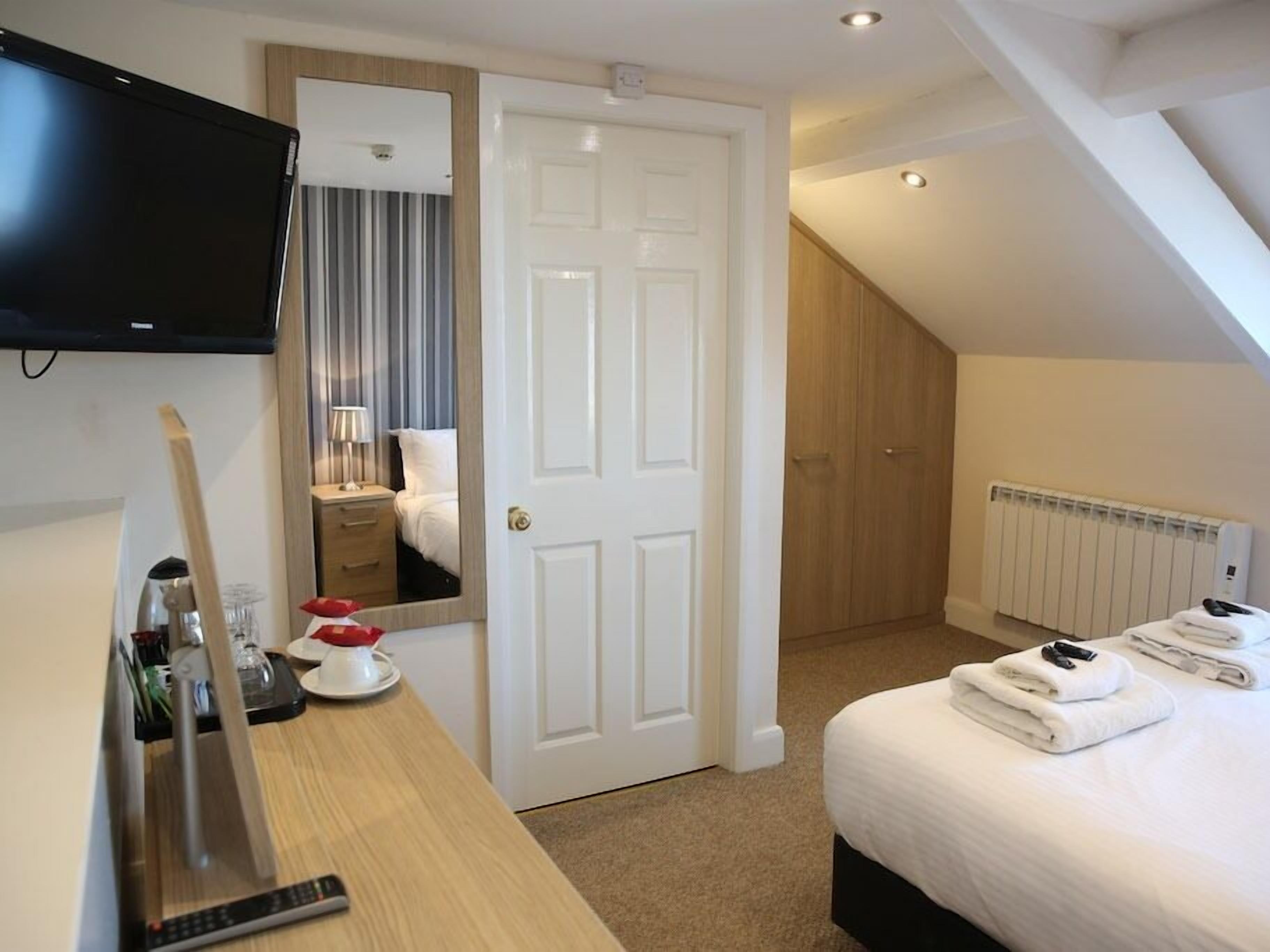 A hotel room with a bed, a desk with a television, a mirror, a radiator, and a door.