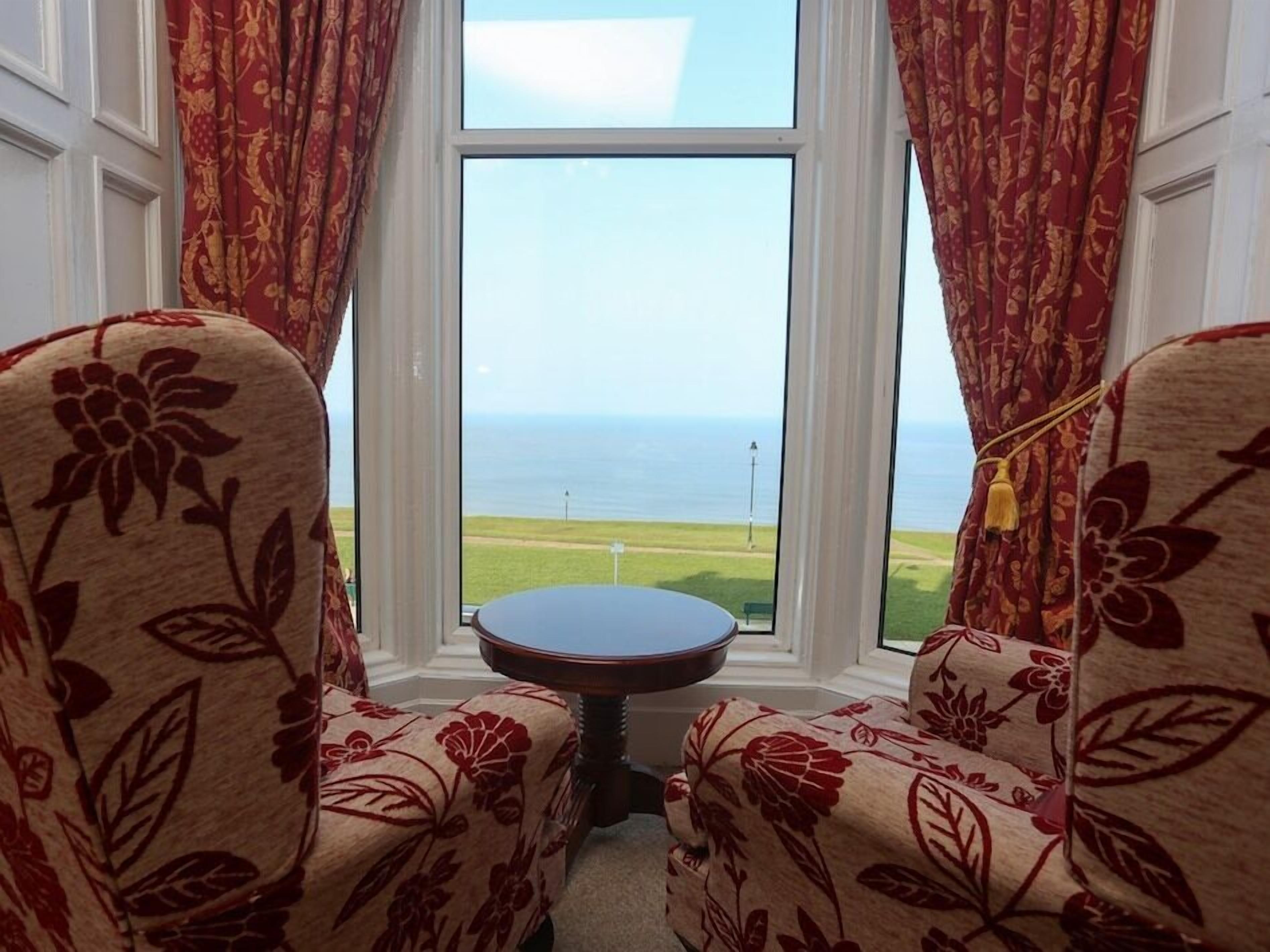 A room with two floral-patterned armchairs facing a window with a view of the sea.