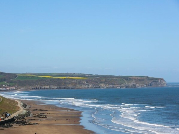 A coastal landscape with a sandy beach, cliffs, and a clear sky.